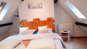 Een slaapkamer met een schuine kap, een houten hoofdbord en een bed met witte beddengoed en decoratieve kussens.