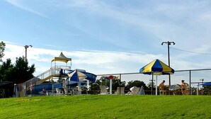 A fenced outdoor area with a playground, including slides and a climbing structure, and several beach umbrellas. - Cozy Home w/ Doggy Fence (Warsaw)