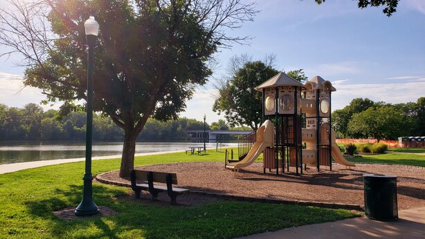 A park with a playground, a bench, a lamppost, and a view of a lake. - Cozy Home w/ Doggy Fence (Warsaw)