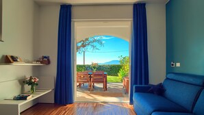 A modern living room with a blue sofa, wooden flooring, a dining table with chairs, and a view of a garden through a glass door. - House with private garden, pool, jacuzzi and electric bikes (Bordighera)
