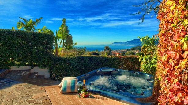 A hot tub with a scenic ocean view, surrounded by lush greenery and a stone deck. - House with private garden, pool, jacuzzi and electric bikes (Bordighera)