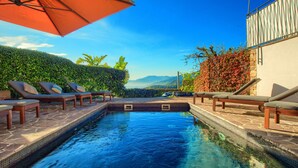 A swimming pool with lounge chairs and an umbrella, surrounded by greenery and a view of mountains. - House with private garden, pool, jacuzzi and electric bikes (Bordighera)