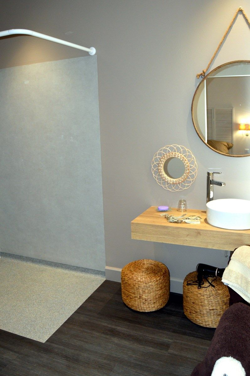 A modern bathroom with a shower, a round mirror, a wooden vanity, and two wicker baskets.