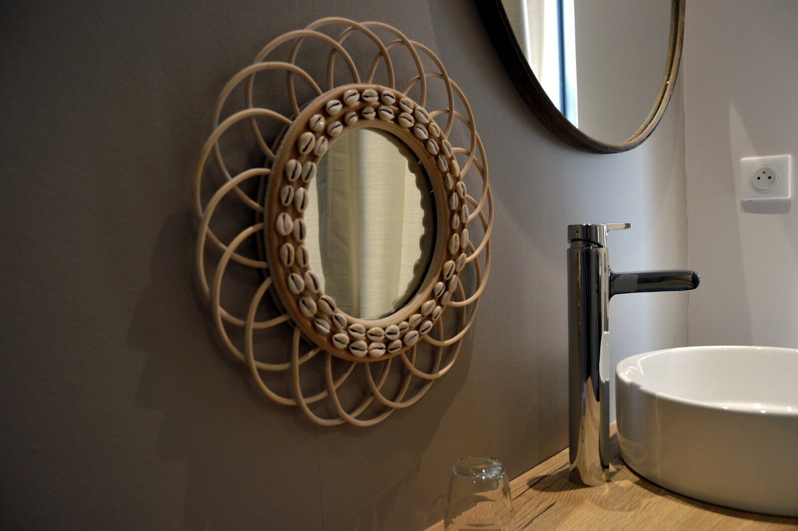 Une salle de bain avec un miroir rond encadré d’un cadre décoratif, un robinet moderne et un lavabo blanc.