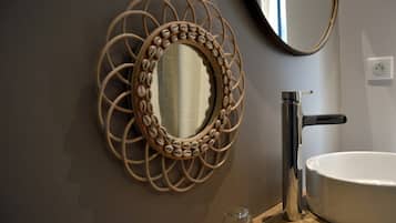 Une salle de bain avec un miroir rond encadré d’un cadre décoratif, un robinet moderne et un lavabo blanc.