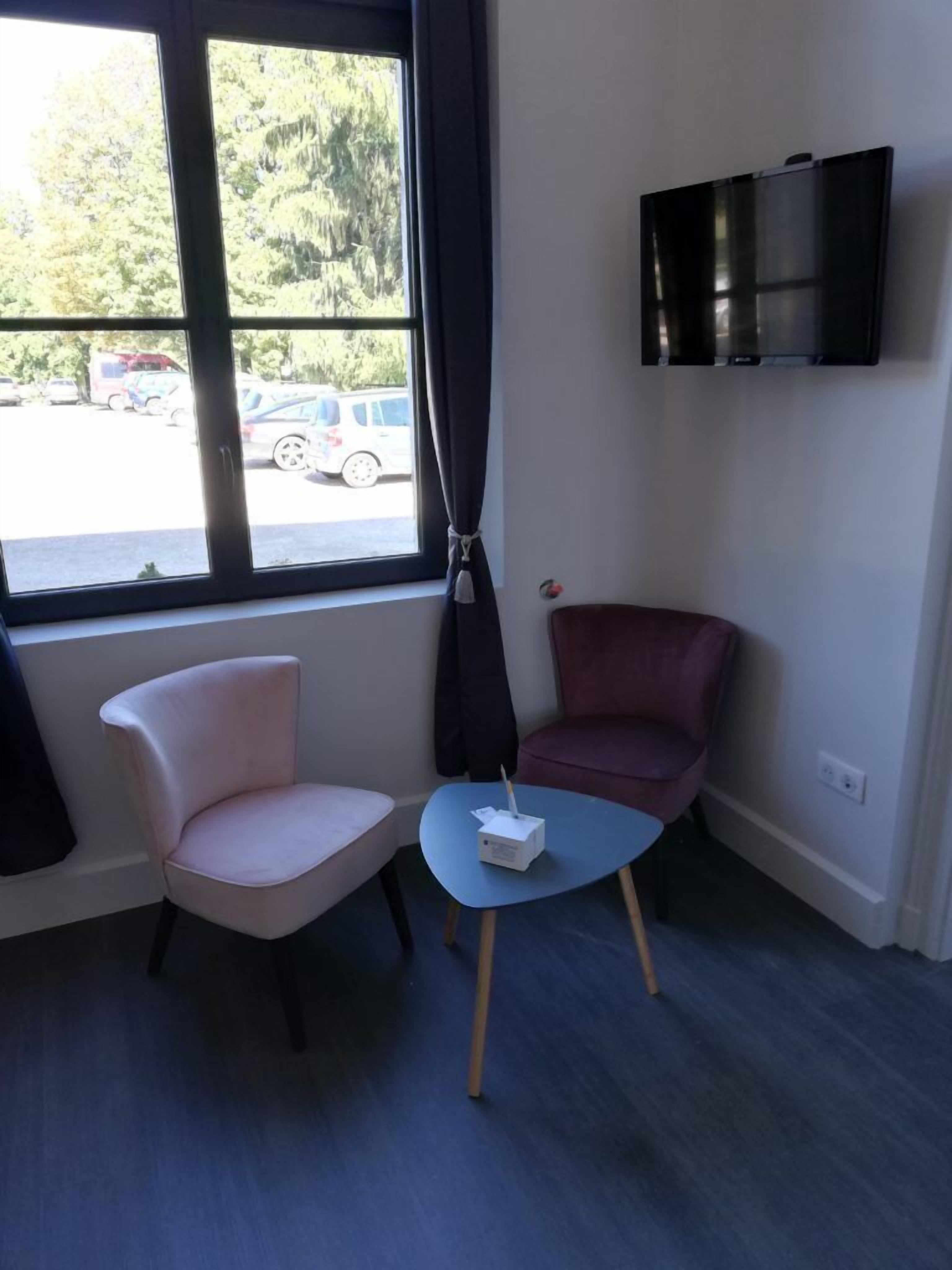 Una habitación con un ventanal grande, una silla rosa, una silla morada y una mesita con un objeto blanco encima.