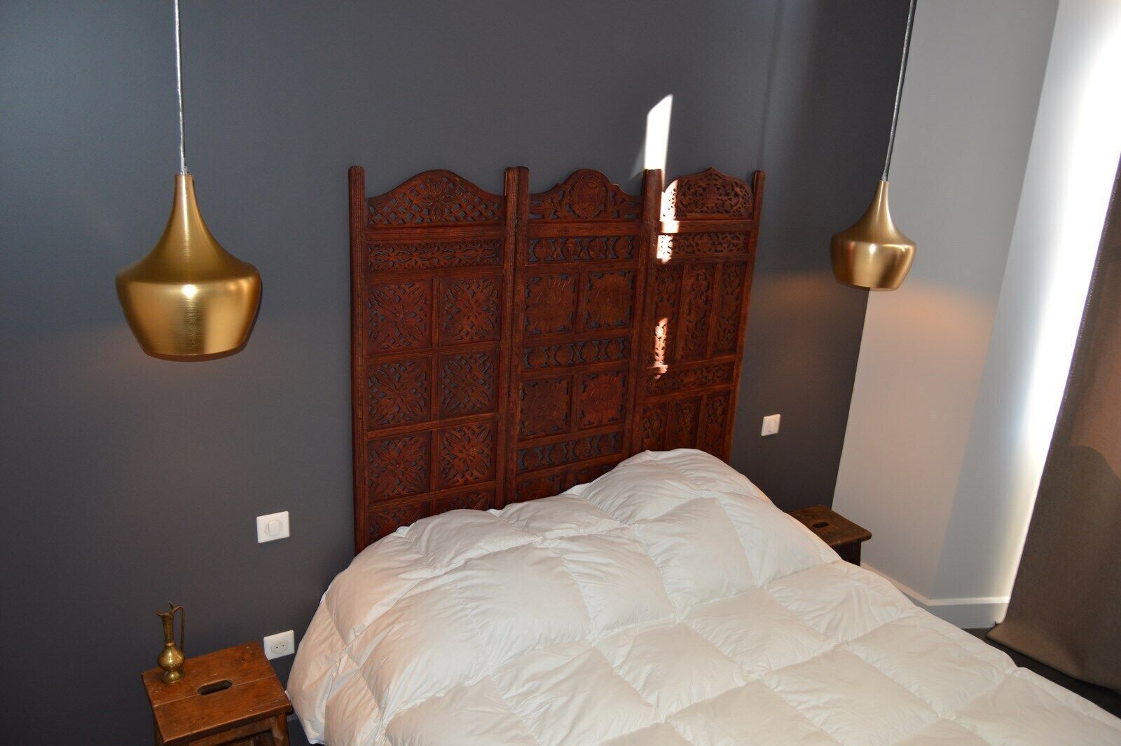 A bedroom with a wooden headboard, a white bedspread, and two brass pendant lights.