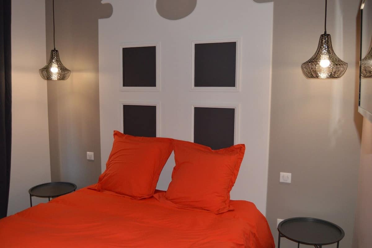 Un dormitorio con una cama, dos almohadas, dos mesitas de noche y dos lámparas colgantes.