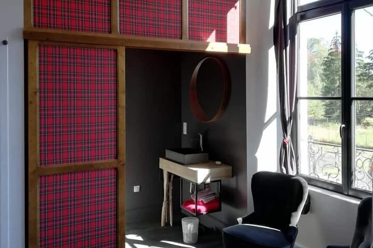 Una habitación moderna con un banco incorporado, un espejo redondo, un lavamanos pequeño y un ventanal con vistas a zonas verdes.