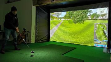 Una persona jugando golf en un interior, con una pantalla grande que muestra un campo de golf.
