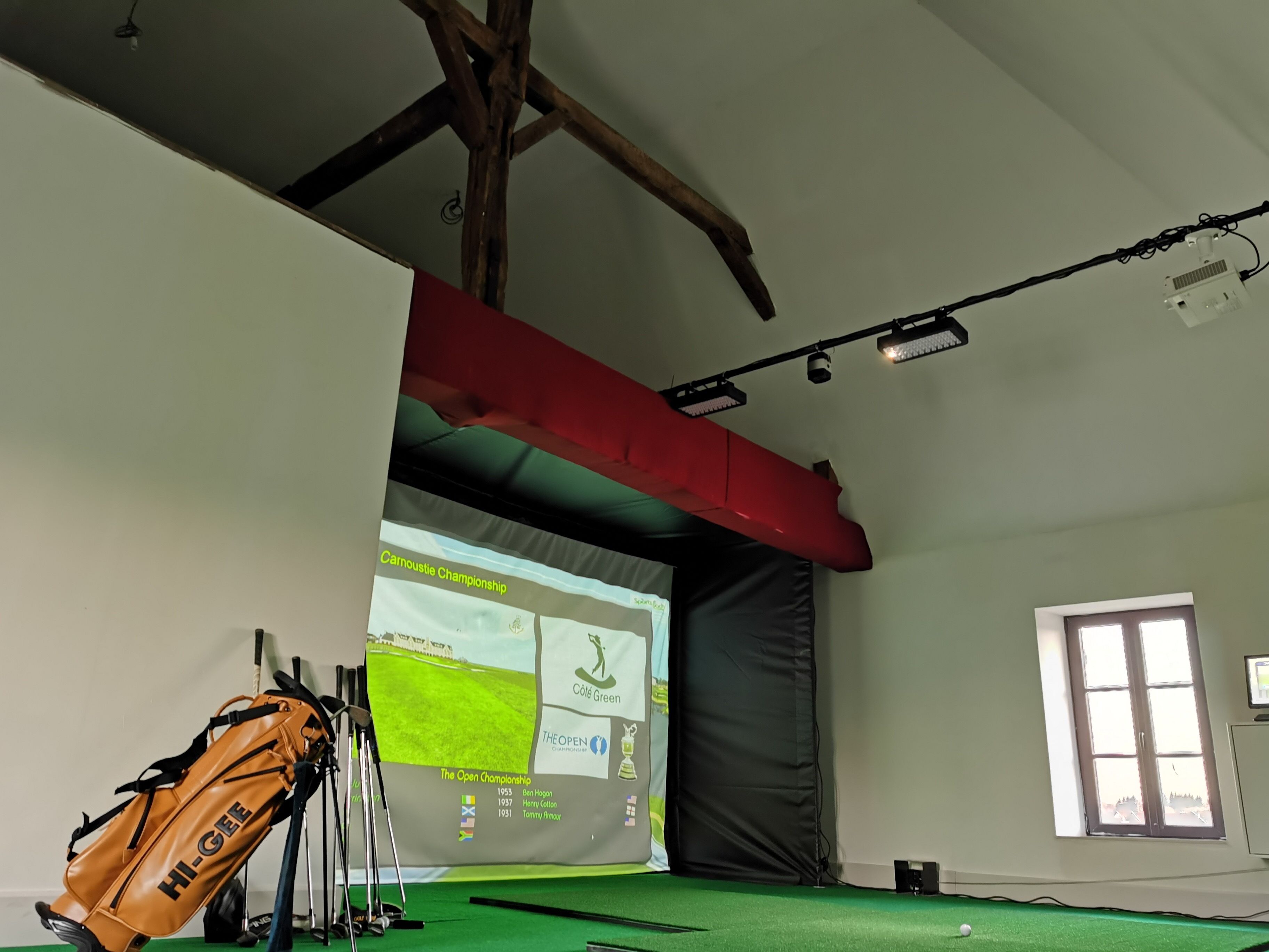 Et værelse med et grønt tæppe, en golftaske og et banner, der viser golf turneringer.