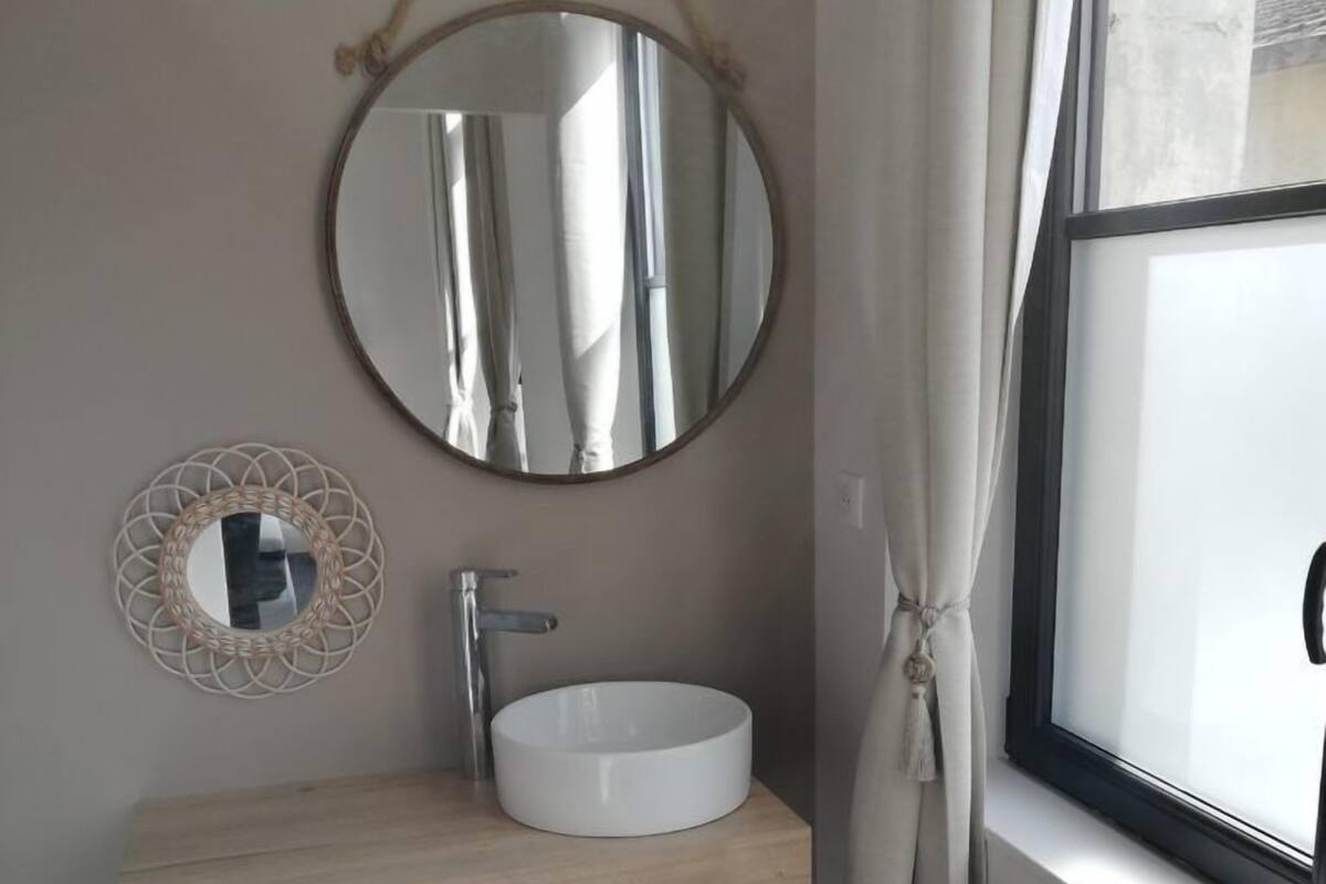 Un baño con un espejo redondo, un lavamanos blanco, un mueble de tocador de madera y dos cestas tejidas.