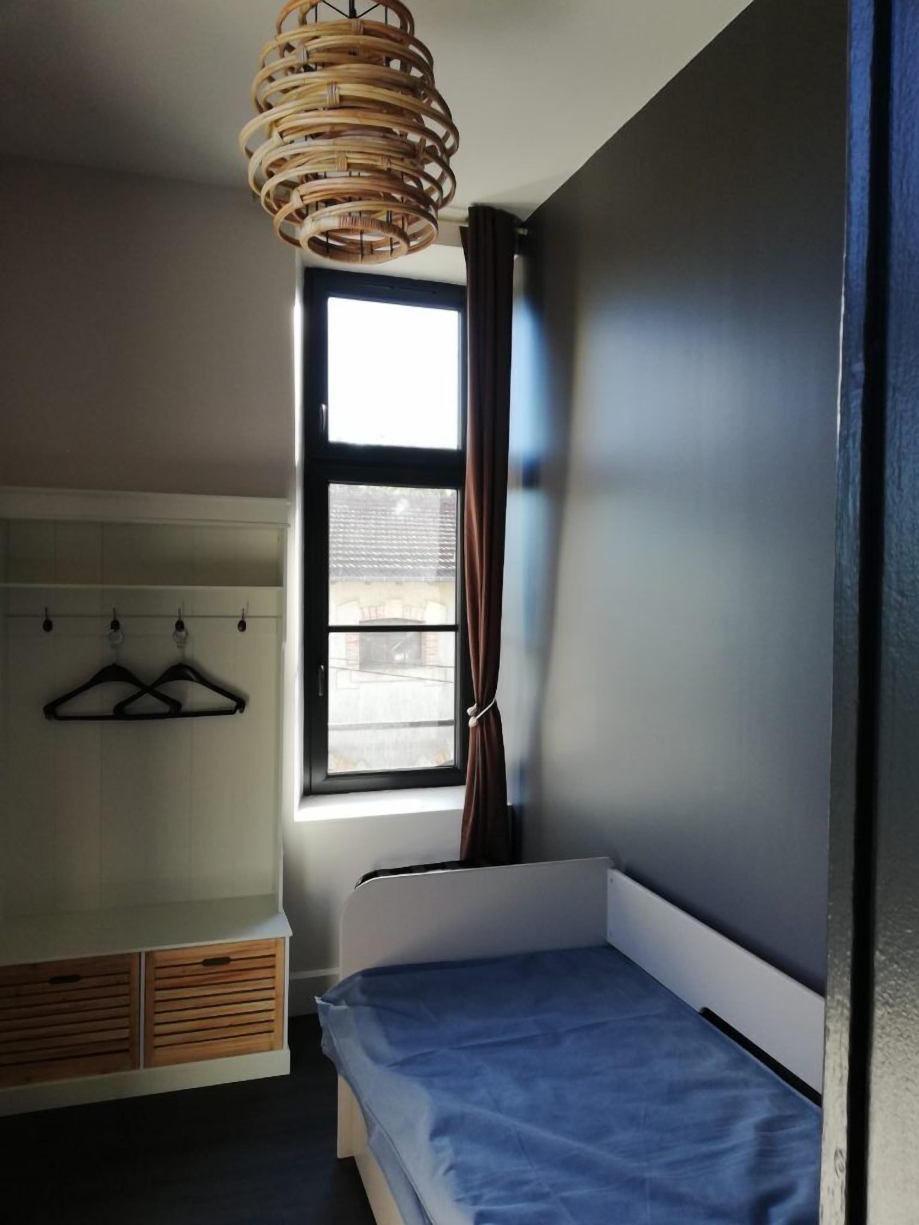 Un dormitorio con una cama individual, una ventana con cortinas, un armario y una lámpara colgante.