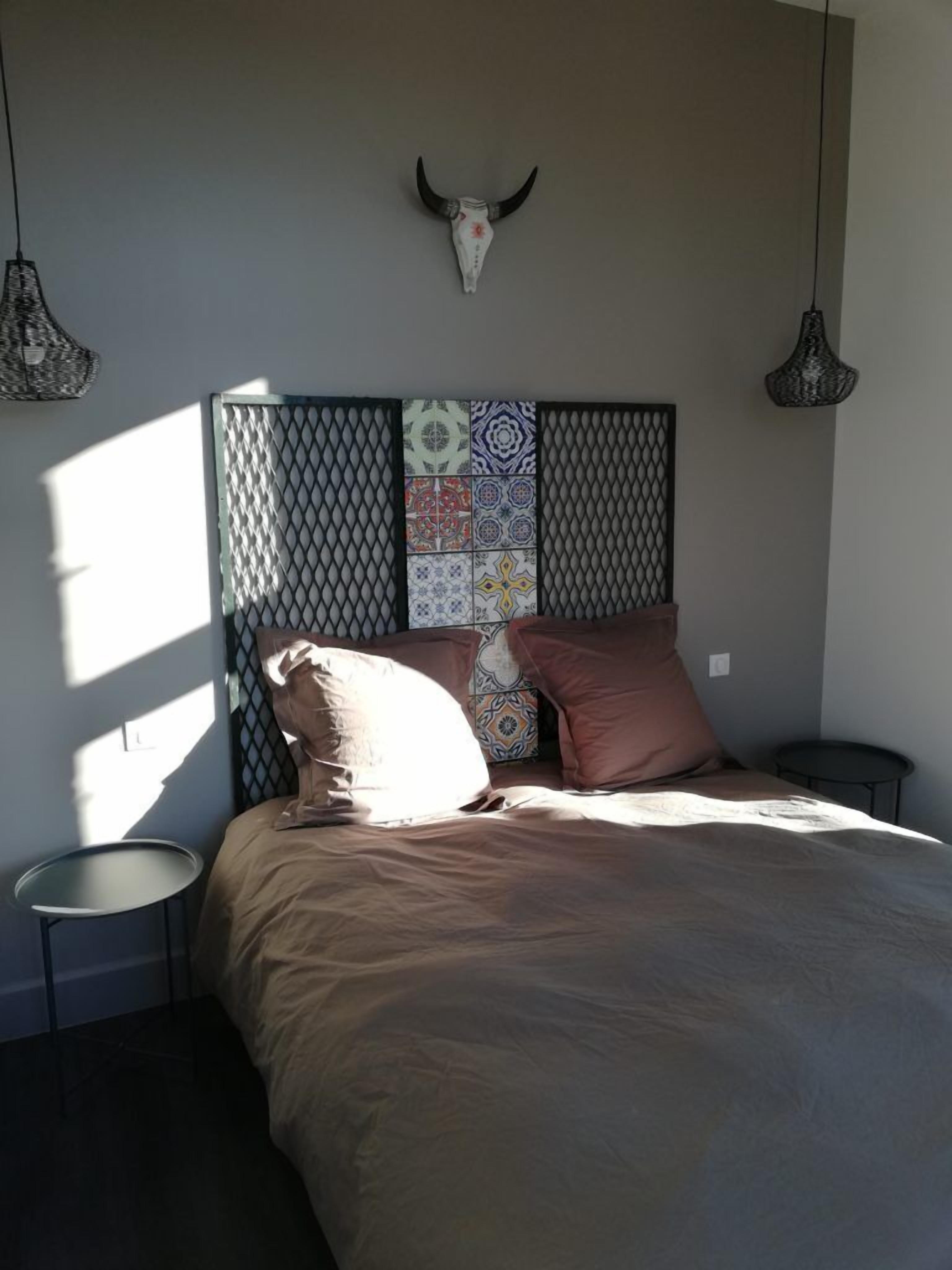 Un dormitorio con cama, almohadas, un cabecero decorativo y un cráneo de vaca colgado en la pared.