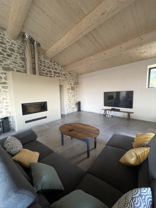 Un salon moderne avec un mur en pierre, une cheminée, un téléviseur à écran plat et un canapé d’angle.