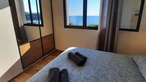 A bedroom with a large bed, a view of the sea through a window, and a sliding door. - Beachfront villa. (Sartène)