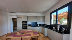 A modern kitchen with a dining area, featuring a large window, built-in appliances, and a tiled floor. - Beachfront villa. (Sartène)