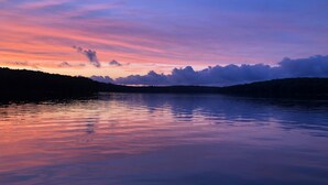 Um lago tranquilo ao pôr do sol, com o perfil das colinas ao fundo.