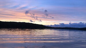 Um lago tranquilo ao pôr do sol, com o contorno de uma colina arborizada ao fundo.