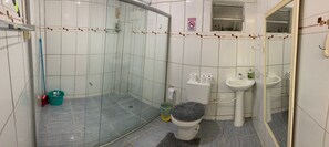 Uma casa de banho com chuveiro em cabine de vidro, sanita, lavatório e espelho.