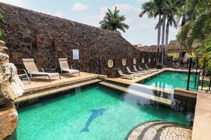 A swimming pool with lounge chairs, a stone wall, and palm trees. - Private 2BR Villa, Resort Pool, Walkable to Beach (Tamarindo)