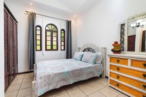 A bedroom with a bed, a dresser, a mirror, and a window with curtains. - Private 2BR Villa, Resort Pool, Walkable to Beach (Tamarindo)