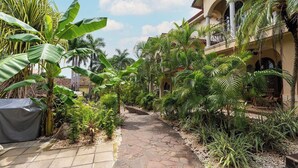 A paved pathway flanked by lush tropical plants, leading to a building with a balcony. - Private 2BR Villa, Resort Pool, Walkable to Beach (Tamarindo)