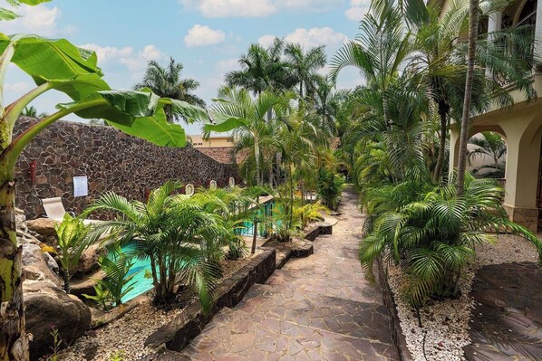 A stone pathway leading to a pool surrounded by lush tropical plants and a stone wall.