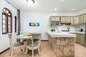 A kitchen with a stone island, wooden cabinets, a microwave, and a dining area with chairs and a table. - Private 2BR Villa, Resort Pool, Walkable to Beach (Tamarindo)