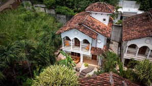 A white building with a red-tiled roof, surrounded by lush greenery.
