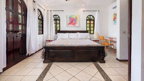 A bedroom with a large bed, two bedside tables, a chair, and a window with curtains.