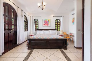 Een slaapkamer met een groot bed, twee nachtkastjes, een stoel en een raam met gordijnen.