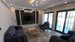 Una sala de estar moderna con un televisor de pantalla plana, dos sofás, una mesa de centro y ventanas grandes.