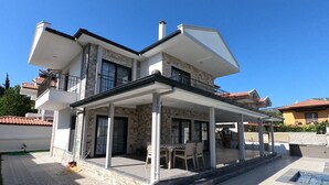 Una casa de dos pisos con un porche cubierto, fachada de piedra y una piscina.