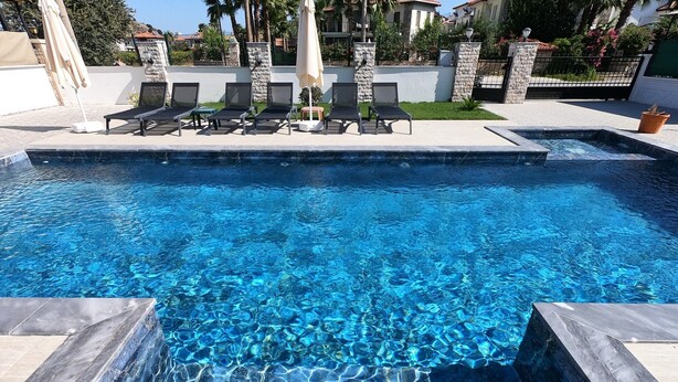 Una piscina con agua cristalina azul, rodeada de sillas de descanso y sombrillas.