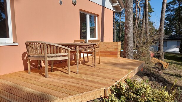 Une terrasse en bois avec une table et des chaises, une fenêtre et une porte.