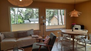Un salon moderne comprenant un canapé, une table à manger avec des chaises, une lampe sur pied et de grandes fenêtres équipées de stores.
