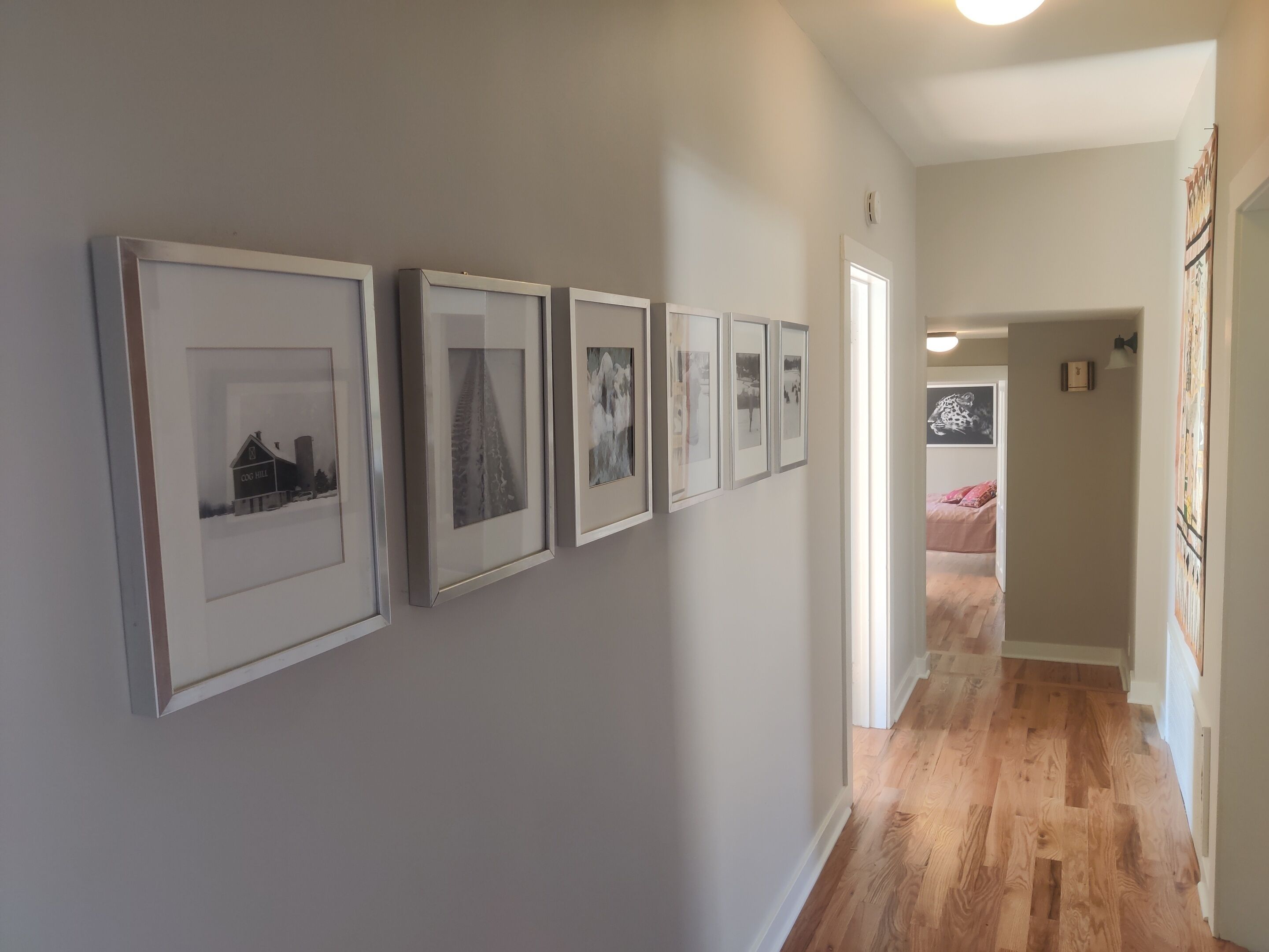 Een gang met ingelijste foto's aan de wand en een houten vloer.