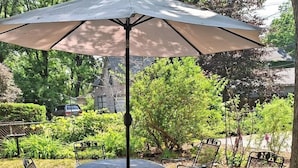 Un patio con una mesa redonda de metal y cuatro sillas, una sombrilla y un suelo de baldosas de piedra.