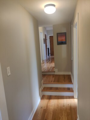 A hallway with a wooden floor, white walls, and a ceiling light.