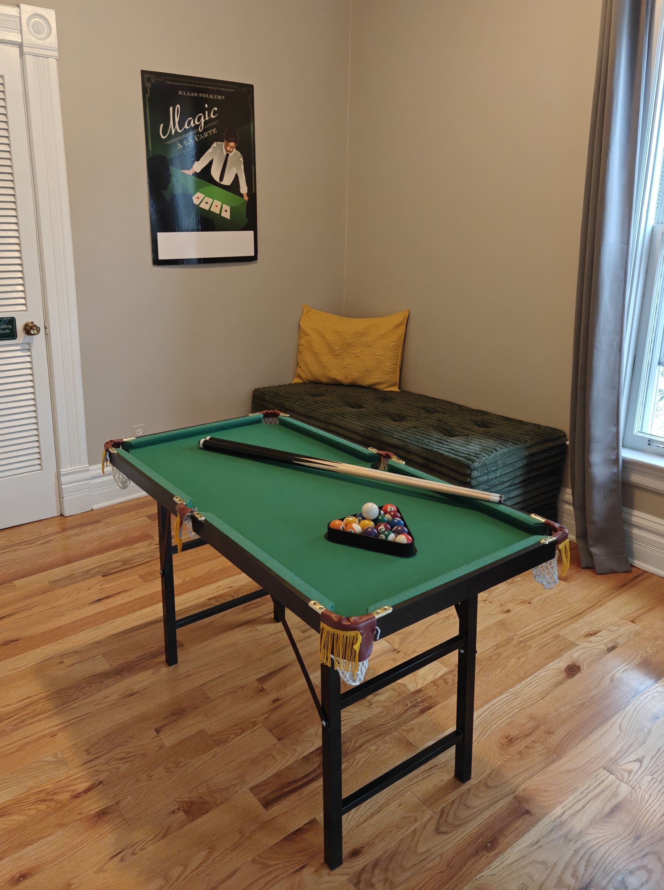 A pool table with balls, a yellow pillow, and a poster on the wall.