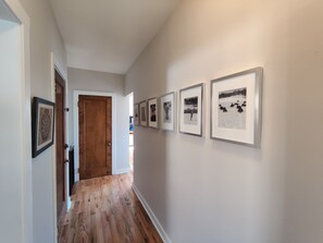 Een gang met houten vloer, een houten deur en een reeks ingelijste foto’s aan de muur.