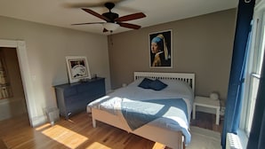 Un dormitorio con cama, cómoda, ventilador de techo, un cuadro enmarcado y ventana.
