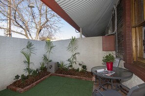 En terrasse med et lille bord og stole, omgivet af krukker med planter og græstæppe.