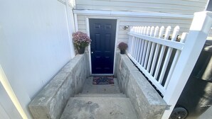 Una escalera de concreto lleva a una puerta azul oscuro con una cerca de piquetes blancos a la derecha.