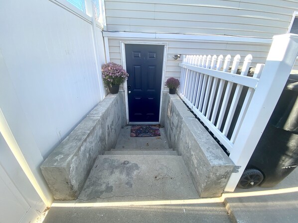 A concrete staircase leading to a dark blue door with a white picket fence on the right.