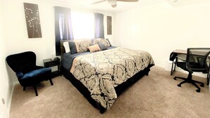 Un dormitorio con cama, escritorio, silla, ventilador de techo y una pared decorada.