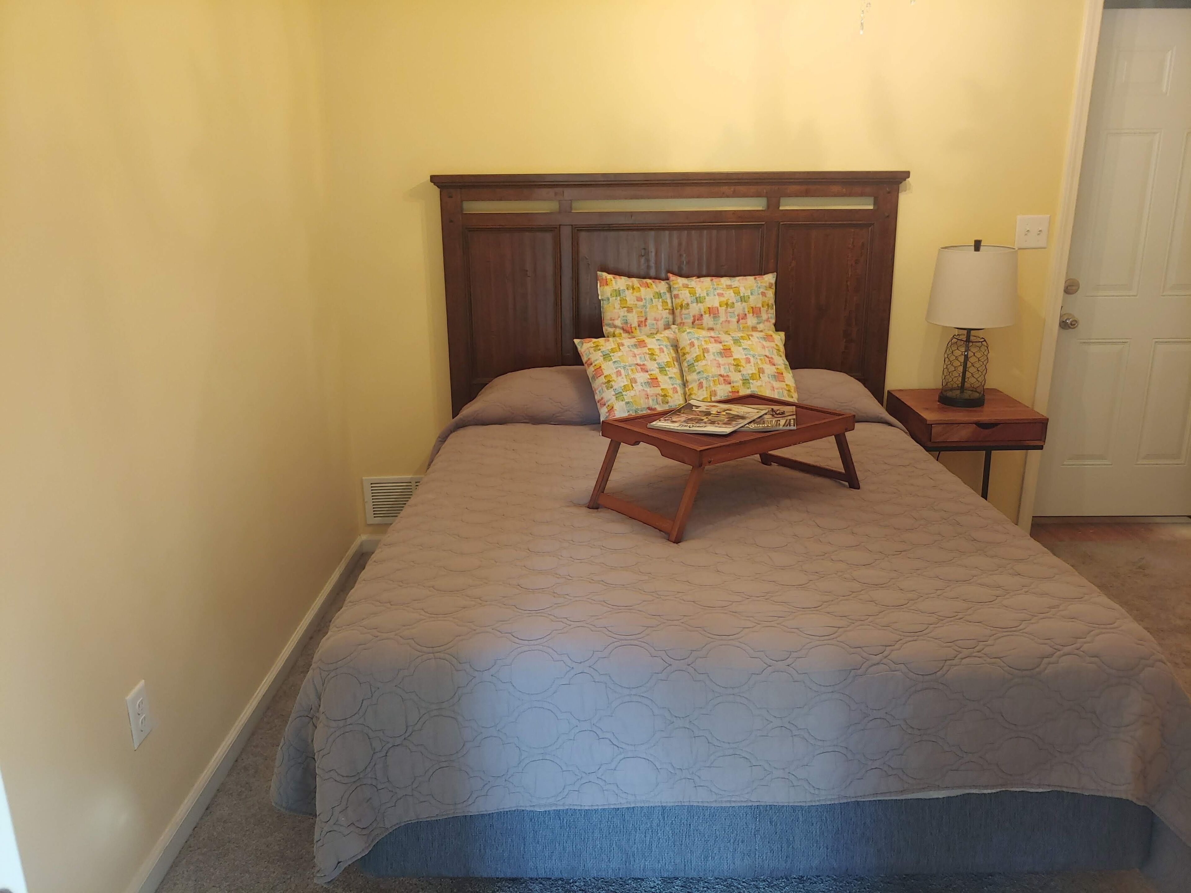 A neatly made bed with a patterned bedspread, two pillows, and a tray with magazines.