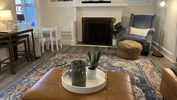 A living room with a fireplace, a television, a dining area, and a seating area with a chair and ottoman. - Charming 4 Bedroom Cottage in Lakeside w/ 4 person golf cart and linens  (Lakeside Marblehead)