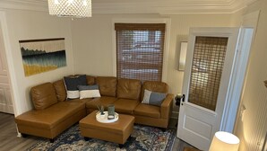 A living room with a brown sectional sofa, a patterned rug, and a small table with a lamp. - Charming 4 Bedroom Cottage in Lakeside w/ 4 person golf cart and linens  (Lakeside Marblehead)